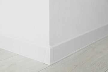 White plinth with connector on laminated floor near wall indoors, closeup