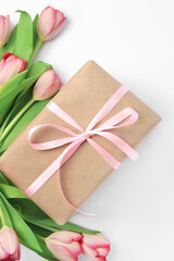 Beautiful gift box with bow and pink tulips on white background, flat lay