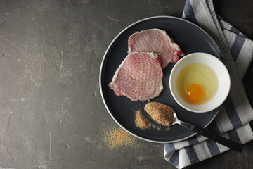 Plate with different ingredients for cooking schnitzel on grey textured table, top view. Space for text