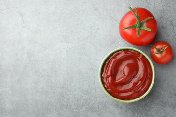 Bowl of tasty ketchup and tomatoes on light grey table, flat lay. Space for text