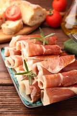 Rolled slices of delicious jamon with rosemary on wooden table