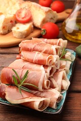 Rolled slices of delicious jamon with rosemary on wooden table