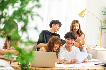 Group of Young Asian man and woman university college students using laptop computer for research and brainstorming discussion analyze ideas making project report together in living room at home.