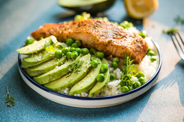 Poke bowl with rice, salmon,avocado and peas, sesame seeds on blue background