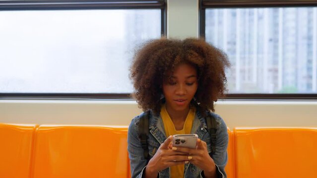 Black young woman, using smart phone and smile in skytrain. Happy african student, young female chatting and typing text message on mobile