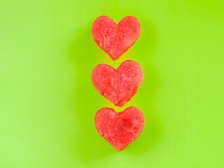 Row of three ripe watermelon slices in shape of hearts on light green background.