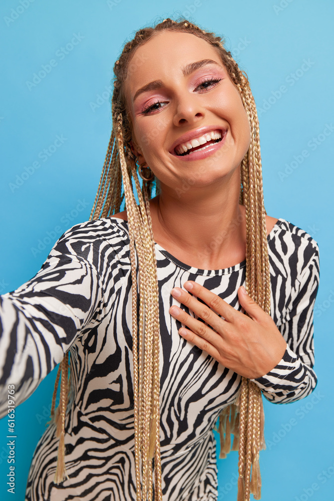 Wall mural Portrait of happy young woman with long fair hair in zebra print top, laughing with one hand on her chest while taking selfie, happy moment concept, copy space - Wall murals