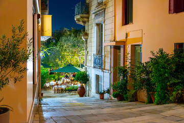 An illuminated sidewalk cafe at night in the Anafiotika neighborhood of the Plaka, underneath Acropolis Hill in the historic center of Athens, Greece.