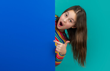 amazed kid behind blank blue paper with copy space for advertisement. point finger