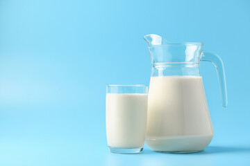 Glass and pitcher of fresh milk on  light blue background.