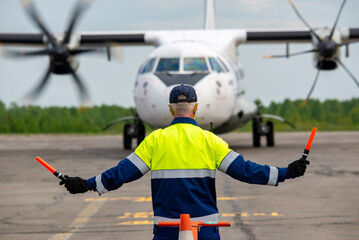 Rear view A signalman meets a passenger plane at the airport in front of propeller airplane. The...