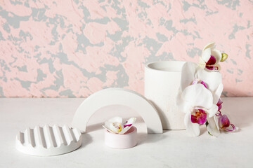 Decorative plaster podiums and beautiful orchid flowers on white table near pink wall