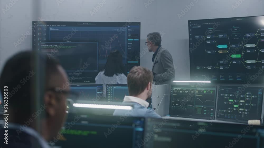 Wall mural mature big data scientist with female colleague analyze real-time charts displayed on multiple big s