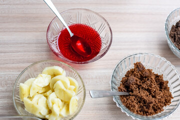 Ingredients of sundae dish as a part of non fire cooking which includes vanilla ice cream, brownie, coco powder, freshly chopped fruits and strawberry syrup. Preparation of sundae dish
