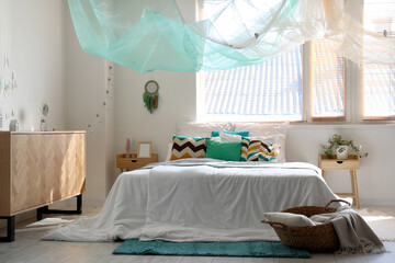 Interior of modern bedroom with bed, chest of drawers and dream catcher hanging on white wall