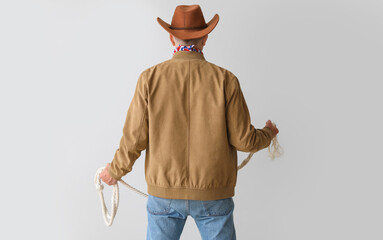 Mature cowboy with lasso on light background, back view - obrazy, fototapety, plakaty