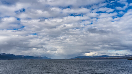 The sea and the blue sky with cumulus clouds. On the horizon, the outlines of a mountain range. Beagle Channel. Argentina.