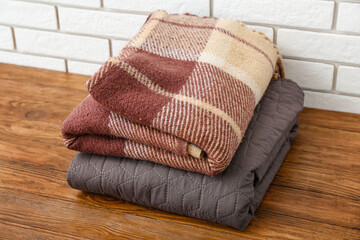 Obraz na płótnie Canvas New soft folded blankets on wooden table near light brick wall