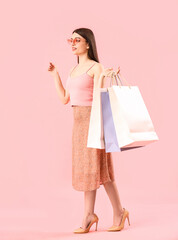 Fototapeta premium Young woman with shopping bags on pink background