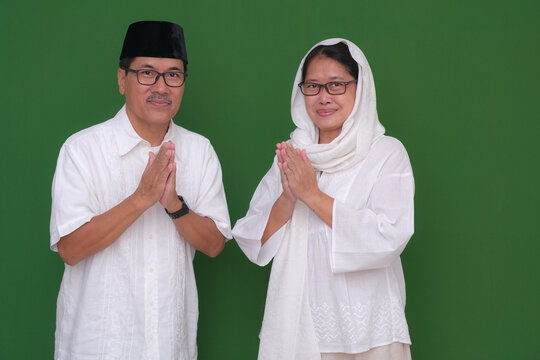 An Asian husband and wife greet others with their hands on their chests.