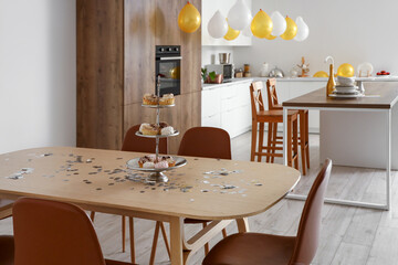 Stand with confectionery and confetti on dining table in kitchen decorated for Birthday party