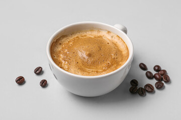 Cup of hot espresso and coffee beans on grey background