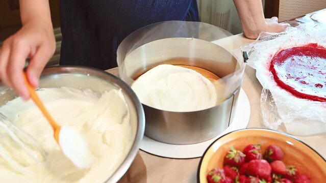 Close-up housewife or pastry chef, confectioner spreading a layer of whipped cream on a baked biscuit sponge cake. Preparing delicious traditional French mousse dessert Fraisier. Confectionery concept