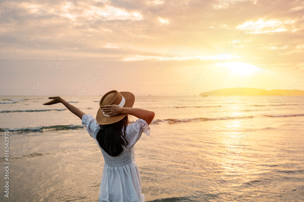 Wall mural young woman traveler relaxing and enjoying the beautiful sunset on the tranquil beach, travel on the - Wall murals
