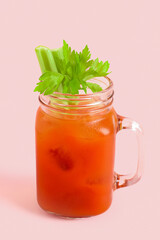 Mason jar of bloody mary with celery on pink background