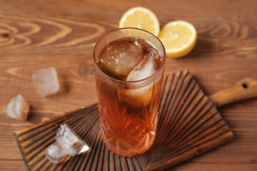 Board with glass of ice tea and lemon on wooden background