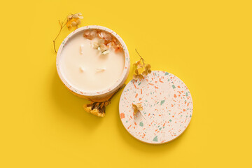 Holder with candle and flowers on yellow background