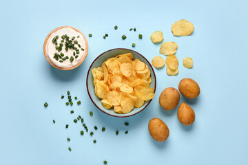 Bowl of tasty sour cream with sliced green onion and potato chips on blue background