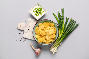 Bowl of tasty sour cream with sliced green onion and potato chips on grey background