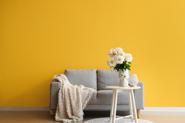 Vase of white peonies with coffee table and couch near yellow wall