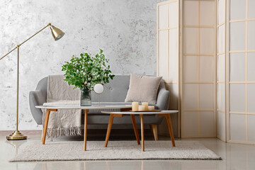 Interior of living room with cozy grey sofa and blooming jasmine flowers on coffee table