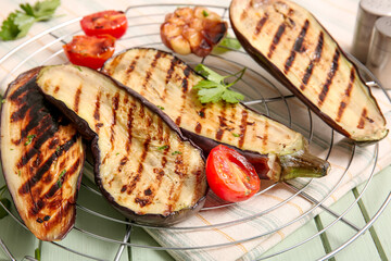 Cooling rack with delicious grilled eggplants and tomatoes on wooden background, closeup