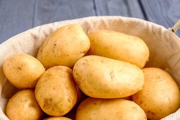 Basket with raw baby potatoes on blue wooden background, closeup