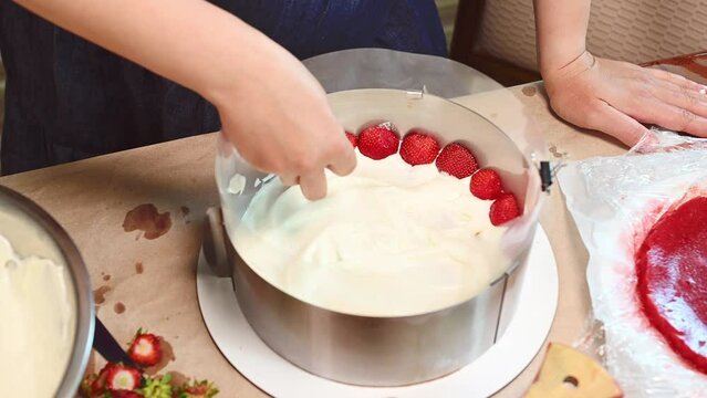 French sweet summer dessert. Fraisier mousse cake. Strawberry cake with biscuit, mousse and jelly. Close-up top view of a housewife putting halves of fresh ripe organic strawberries on the top of cake