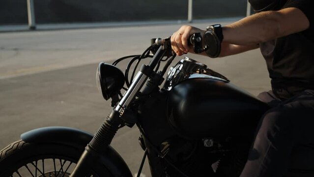 A motorcycle and a man in the summer. Black clothes on a biker and a shiny black motorcycle. Rare motorcycle. Backlight on the bike. Motorcycling as a hobby. A man's hand pedals the gas on a bike. A
