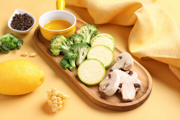 Wooden board with fresh vegetables on yellow background