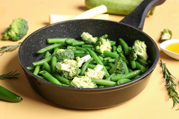 Frying pan with fresh vegetables on yellow background