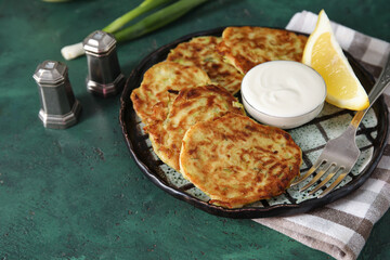 Plate with tasty zucchini fritters on green background