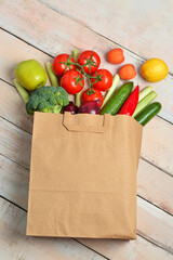 Paper bag with fresh vegetables and fruits on light wooden background