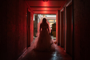 A ghostly woman in torn wedding dress walks along a dark haunted hotel hallway, red light....