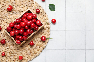 Wooden box with sweet cherries on white tile background