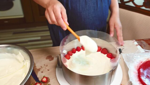 Close-up housewife making strawberry summer mousse cake Fraisier in home kitchen. Epicure. Bakery confectionery. Cuisine. Traditional French patisserie. Putting whipped cream on the sponge cake