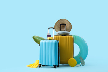 Suitcases with inflatable ring, passport and beach accessories on blue background. Summer vacation...