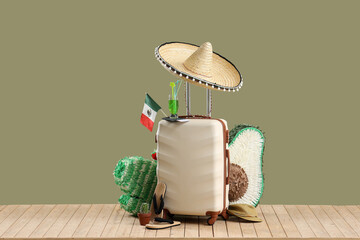 Suitcase with Mexican flag, pinatas, beach accessories and cocktail on wooden pontoon against green background. Travel concept - obrazy, fototapety, plakaty