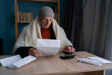 Freezing old man holding bills for electricity, gas and heating, calculating it. Global energy...