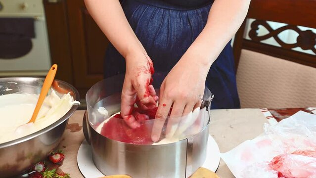 Close-up housewife's hands putting layer of strawberry jelly on cake while preparing a french light mousse summer dessert -Fraisier. Confectionery. Traditional light sweet dessert. French patisserie